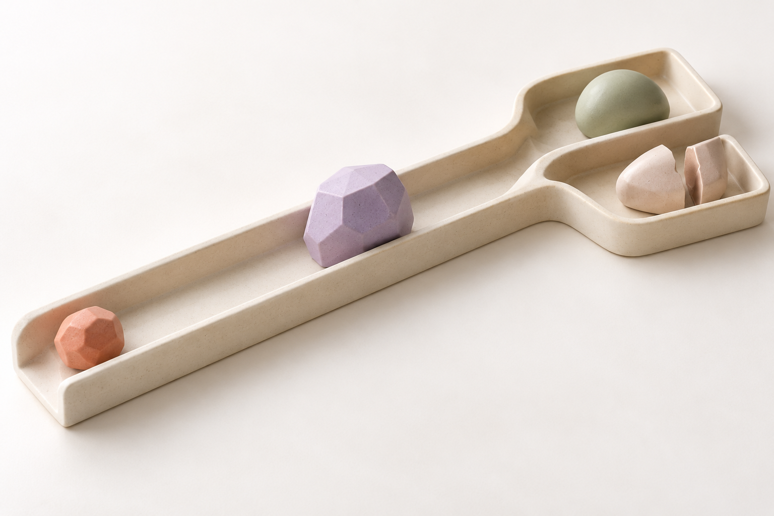 クリーム色の長い溝が二つの受け皿へ分かれ、途中の紫色の部品の先に、完成した緑色の形と分離した二片がある。